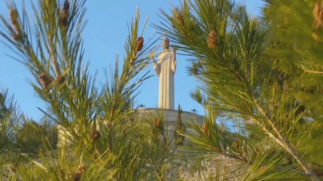 pine tops swaying in the wind, against the blue sky and the statue of Christ between the branches. Palencia, North Spain. No sound.