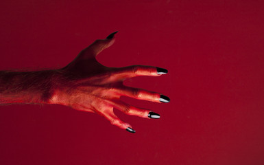 Halloween red devil monster hand with black fingernails against a red background