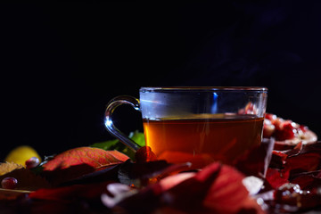 Tazza di té caldo fumante su fondo nero con foglie autunnali