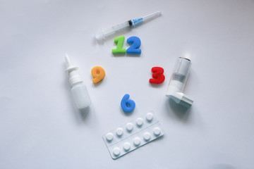 Pills, syringe, inhaler, thermometer, spray and colored numbers symbolizing the clock on a white background