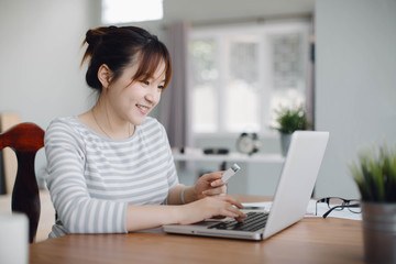 Young woman holding credit card and using laptop computer. Online shopping concept