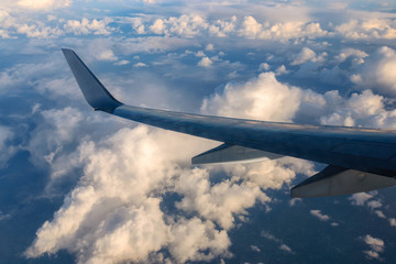 Fototapeta premium View from airplane window to sky with clouds during sunrise. Wing of aircraft flying above clouds
