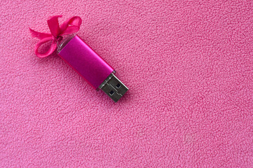 Brilliant pink usb flash memory card with a pink bow lies on a blanket of soft and furry light pink...