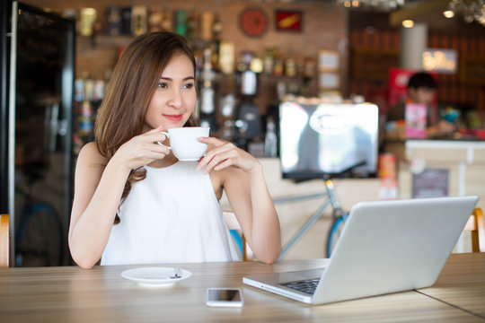 Portrait of young woman drinking coffee and using laptop at a cafe.