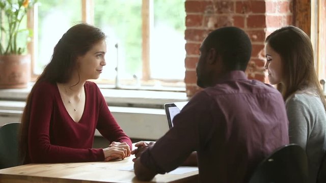 Female applicant introducing herself at job interview, talking about work experience, african and Caucasian hr managers listen to candidate trying to make good first impression, hiring negotiations