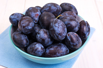 Blue ceramic bowl with plums on white wooden background