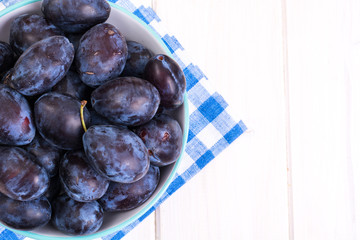 Blue ceramic bowl with plums on white wooden background