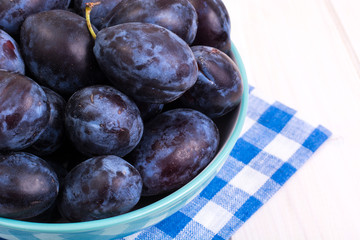 Blue ceramic bowl with plums on white wooden background