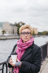 Fototapeta premium Portrait of adult woman with takeaway coffee cup standing on esplanade. 