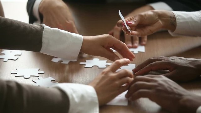 Close up view of business people hands trying to connect assembling jigsaw puzzle and join pieces on conference table in office, team help and support, finding right solutions in teamwork concept