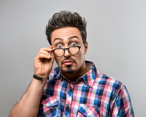 Fototapeta na wymiar Handsome young man Having Fun Crazy. Surprised Gesturing. Portrait Hipster Nerd guy in Trendy shirt, Glasses. Brunette Bearded Emotional Stylish Hairstyle on gray background. Blue Eyes