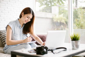 Beautiful young woman taking note while sitting on sofa