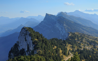 Hiker standing on top of a small, distant peak in the mountains. Vercos, France.