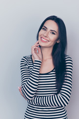 Young adorable entrepreneur in casual clothes on pure grey background with crossed arms, caressing her face, with nice natural light make up, long dark straight hair, smooth nice skin