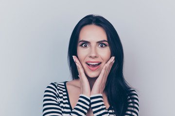 Very excited lady in casual wear, gesturing unbelievable unexpected wonderment, expressing positive emotions, with wide open eyes and mouth, on pure lght grey background, holding her face with arms