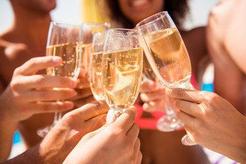 Close up cropped shot of excited cheerful chilling youth celebrating with martini wines, laughing and enjoying, in colorful bikinies, on resort. Sun shines, reflects in drinks