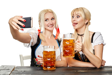 Two beautiful women holding a glass of beer while sitting at a wooden table on a white background in the studio