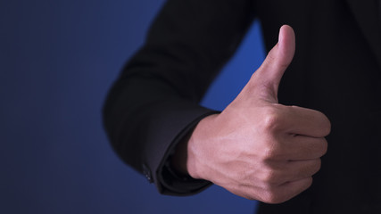 Businessman showing OK sign with his thumb up on blue and black background.