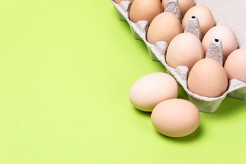 Chicken eggs in a cardboard box on a green background. Copy space for text
