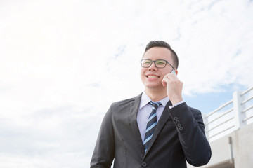 Young asian businessman wearing black suit smiling while talking with someone by mobile phone