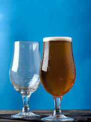 Empty glass and a glass of light beer on a blue background.