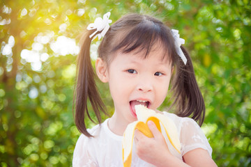 Little asian girl eating banana and smiles between picnic in park