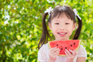 Little asian girl holding watemelon and smiles between picnic in park