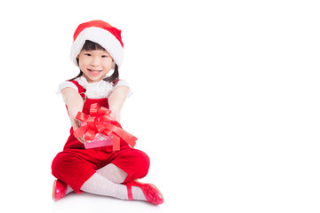 Little asian girl wearing santa claus red dress sitting on the floor holding small gift box and smiles