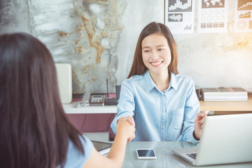 Young asian beautiful businesswoman wearing blue shirt shaking hands with her partner and smiles at office