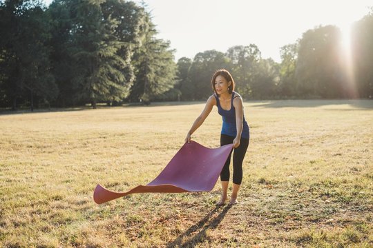 Mature woman in park, laying yoga mat on grass