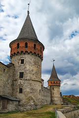 Fototapeta na wymiar Tower of the old Kamianets-Podilskyi Castle under the cloudy blue sky. The fortress located among the picturesque nature in the historic city of Kamianets-Podilskyi, Ukraine.