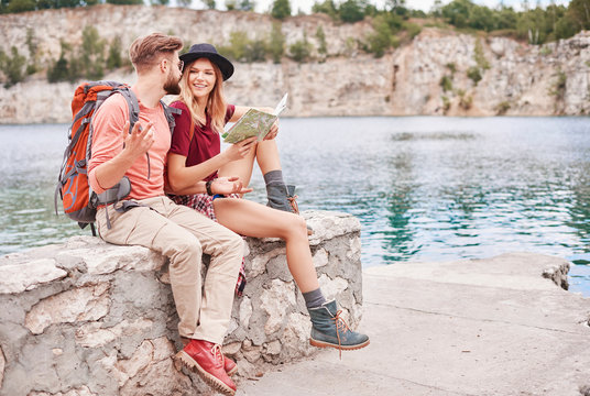 Couple sitting on wall by water looking at map, Krakow, Malopolskie, Poland, Europe
