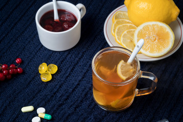 Still life of tea with lemon, tablets and thermometer, jam and berries. The concept of treating colds