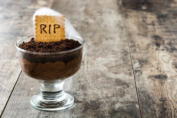 Funny Halloween chocolate mousse with tomb cookie on wooden table
