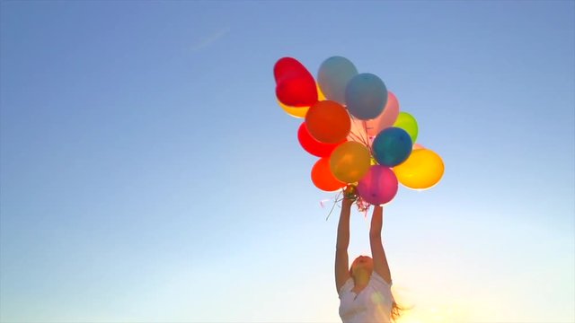Beauty girl with long hair spinning with colorful air balloons over blue sky. Slow motion 4K UHD video 3840X2160