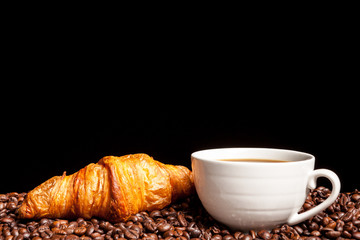 Croissant and coffee beans in close up photo. Delicious morning drink and snack