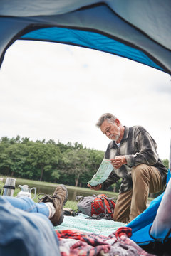 Mature woman relaxing in tent, man outside tent, looking at map