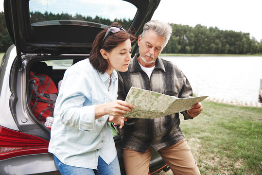 Mature couple in rural setting, standing beside car, looking at map