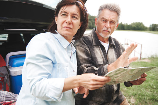 Mature couple in rural setting, standing beside car, looking at map