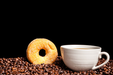 Coffee beans, donut and a cup of coffee in close up photo