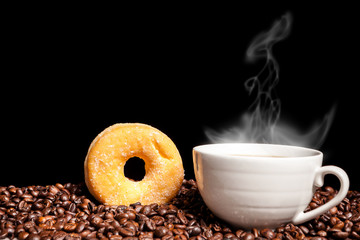 Coffee beans, donut and a steaming cup of coffee in close up photo