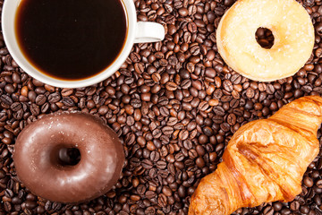 Over top view of Coffee beans, donut and a cup of coffee in close up photo