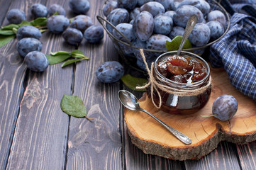 Homemade plum jam in a glass jar and fresh blue plums in a bowl on a dark rustic wooden background...