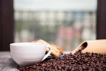 Coffee beans, sweet donut and a cup of coffee in close up photo