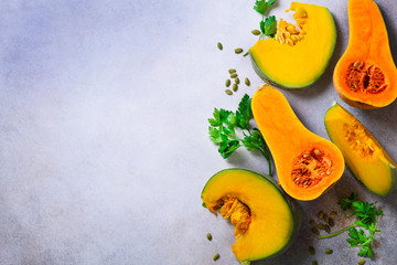 Cut ripe orange pumpkin with seeds and herbs on light grey background. Vegetarian and raw organic healthy food concept, diet. Top view, copy space