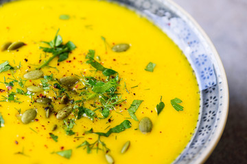 Bright organic pumpkin, lentils and carrot soup with seeds and herbs on light grey background. Copy space, top view