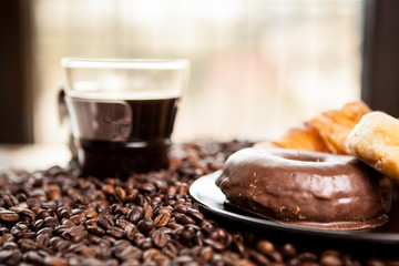 Coffee beans, donut and a cup of coffee in close up photo