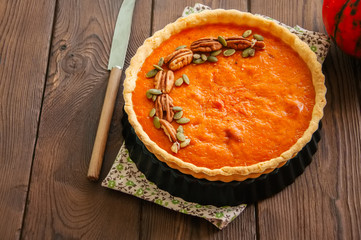 Pumpkin pie garnished with pecans and seeds on a wooden background