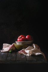 Bowl of tomatoes with pepper and linen towel on old wooden kitchen table. Dark rustic still life.