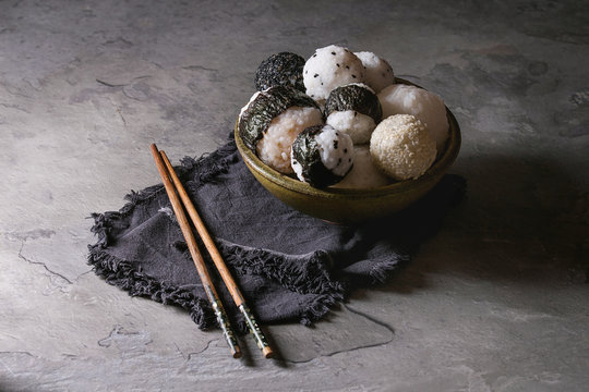 Bowl with different size rice balls with black sesame and seaweed nori, served with soft boiled eggs, soy sauce, chopsticks over gray table. Asian style dinner.